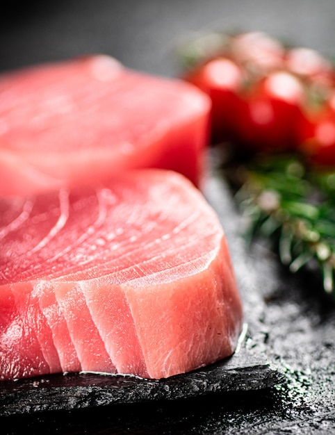 raw tuna on a stone board with rosemary and tomatoes