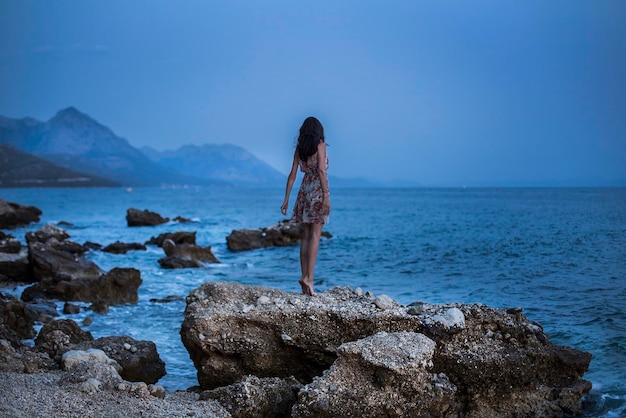 Rear view full length of woman standing on rock at beach