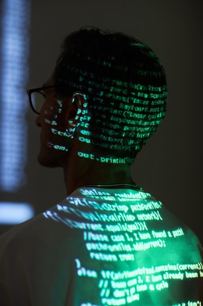 Rear view of computer hacker sitting and reading a computer code reflecting on his back