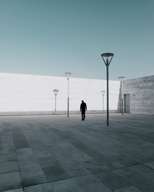 rear view of man walking on footpath in city against clear sky