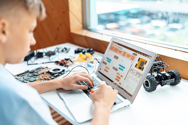 Schoolboy in blue shirt use laptop code robotics car in STEM class Edification