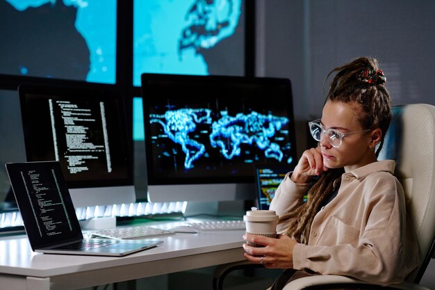 Serious young programmer in eyeglasses looking at laptop screen