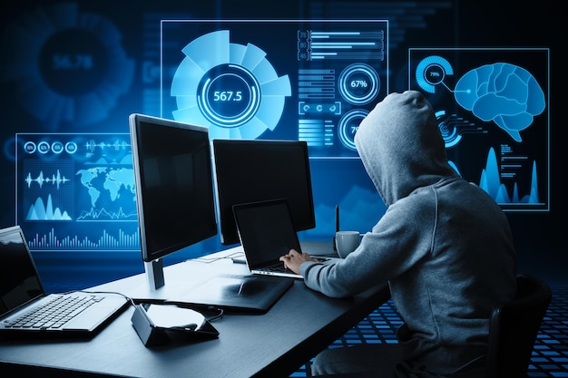 Side view of hacker at desktop using computers with abstract glowing blue business charts and graphs hologram on dark background Innovation hacking future and fintech concept