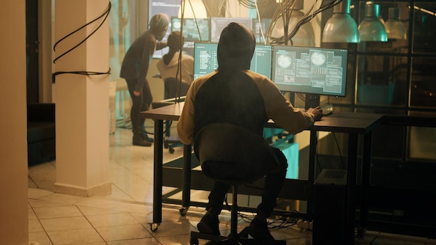 Silhouette of hacker coding encryption to plant trojan virus, looking to steal important information at night. Male thief using computer malware to hack online web network system.