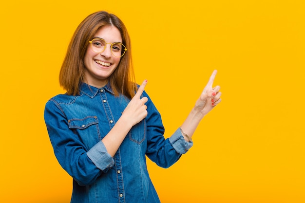 smiling happily and pointing to side and upwards with both hands showing object in copy space