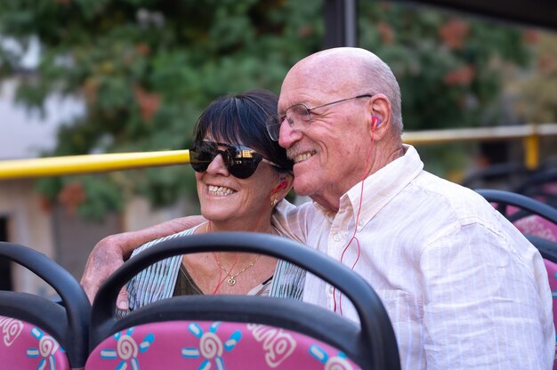 Smiling senior happy caucasian couple sitting on sightseeing open top bus visiting Cordoba