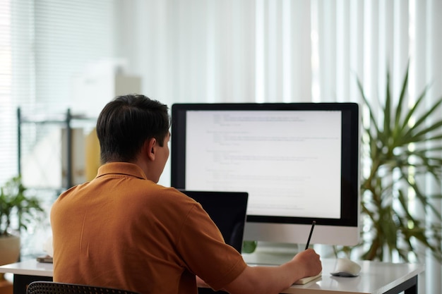 Software developer reviewing programming code and taking notes in planner