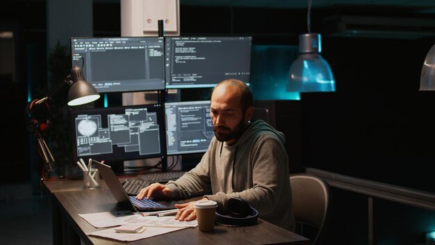 Software engineer typing source code on multiple monitors, displaying terminal window with html language. Programming cloud computing interface on laptop to develop system. Handheld shot.