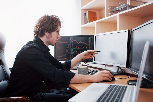 stressful day at the office. young businessman holding hands on his face while sitting at the desk in creative office. stock exchange trading forex finance graphic concept