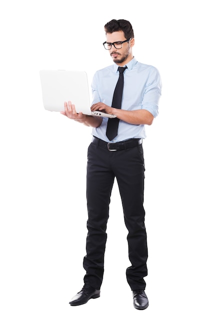 Supporting your business. Full length of handsome young man in shirt and tie working on laptop