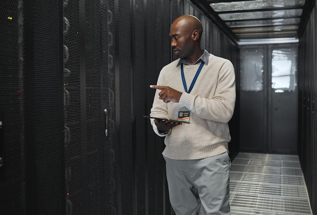 Tablet network management and IT black man for software update working on code in dark server room Computer cybersecurity and male programmer with tech for problem solving or troubleshooting