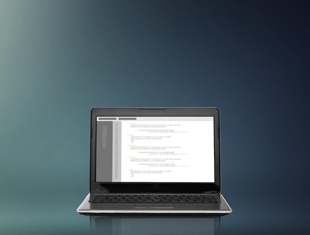 technology and programming concept - laptop computer with coding on screen over gray background