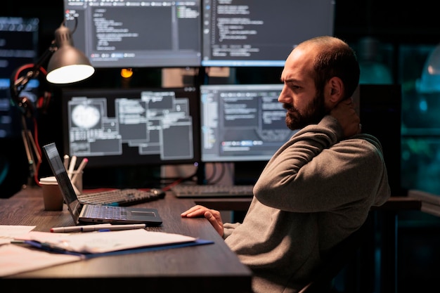 Tense stressed engineer feeling neck pressure and back pain, working after hours at office. Overworked exhausted coder dealing with tension late at night, programming source code.