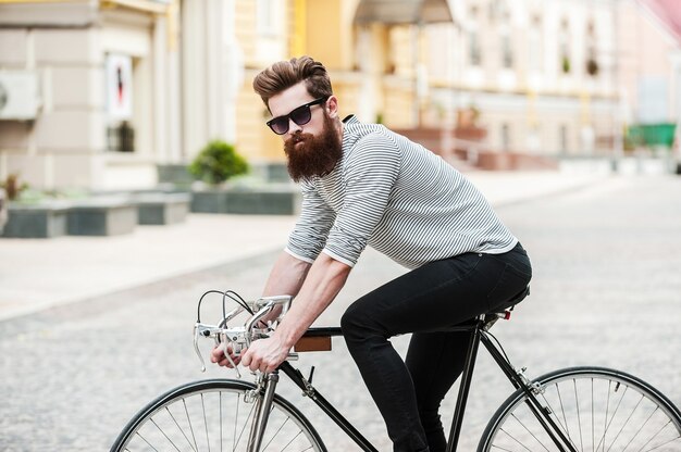 the way with no traffic! side view of handsome young bearded man looking at camera while riding on his bicycle outdoors