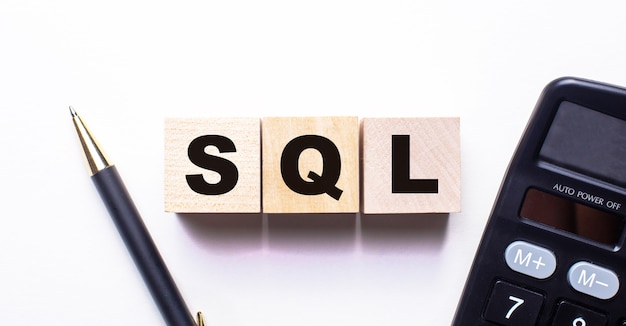 the word sql is written on wooden cubes between a pen and a calculator on a light wall.