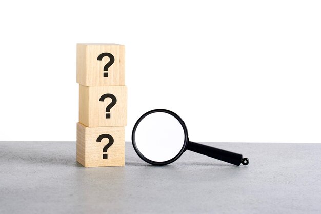 Three question sign on wooden cube with magnifying glass on grey table