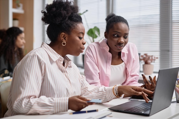 Two black business women talk shop using computer