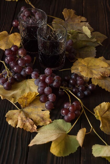 two crystal glasses with red wine, grapes and dry leaves on a wooden surface