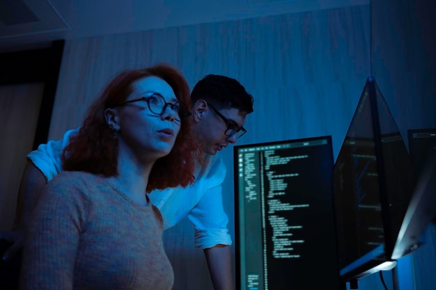 Two software developers collaborating at night focusing on code review and debugging process on a computer screen representing teamwork innovation and modern software development workflow