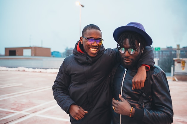 two young african men posing together in the street and looking camera hugging