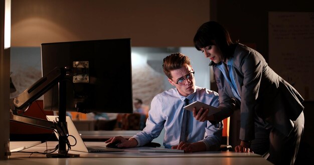 Two young designers are working on a new project in the night office using modern technology