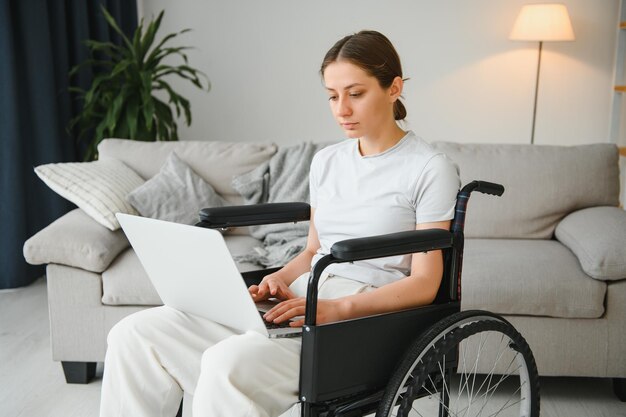 Woman in a wheelchair works on the laptop PC in the home office with an assistance dog as a companion