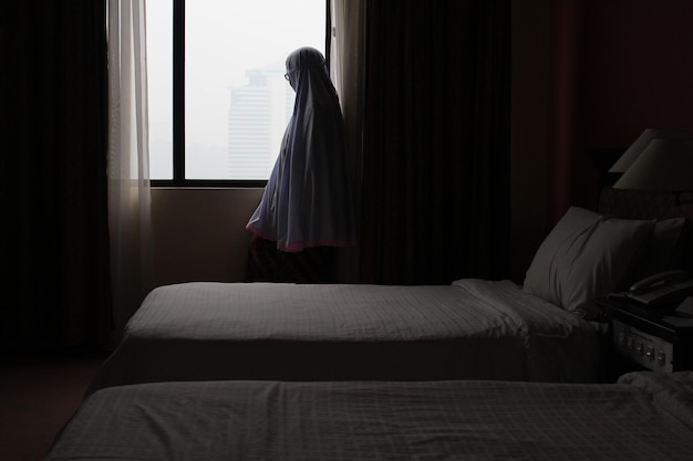 woman looking through window while standing at home