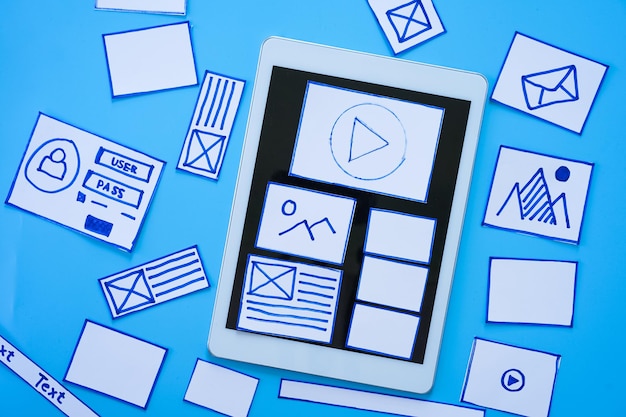 Working desk with hands sorting wireframe screens of mobile responsive website Developing wireframe sketch layout design mockup on smartphonetablet screen