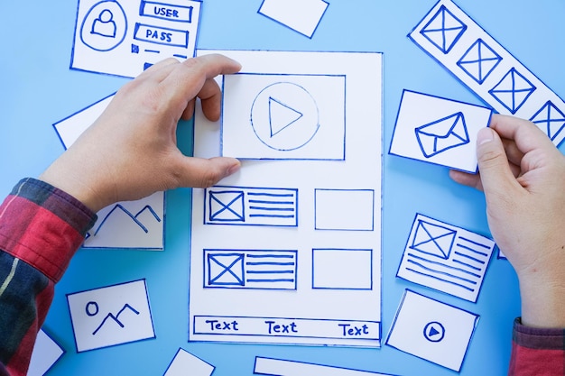 Working desk with hands sorting wireframe screens of mobile responsive website Developing wireframe sketch layout design mockup on smartphonetablet screen