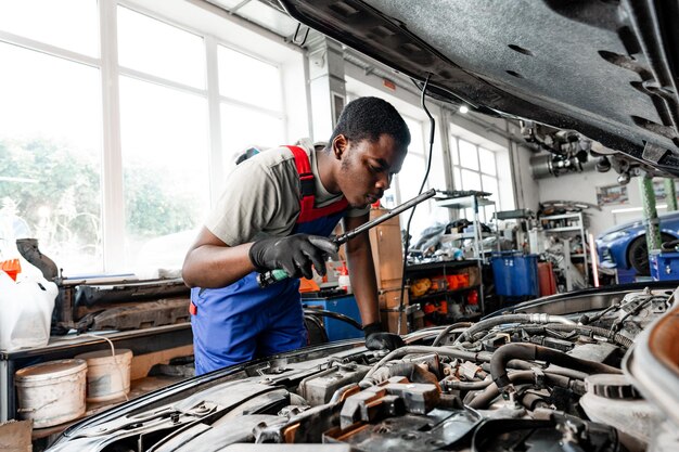 young african auto mechanic checking car engine under the hood in auto service