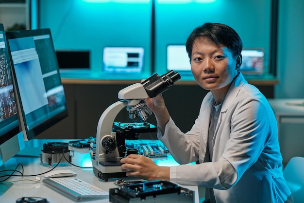 Young asian researcher in whitecoat working with microscope