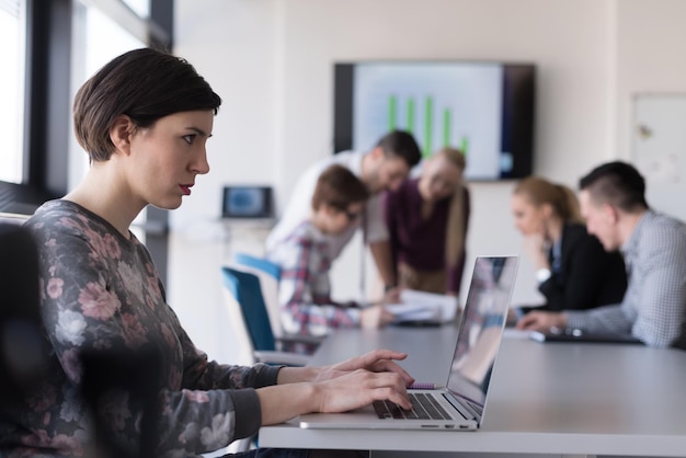 young  business woman at modern startup office interior working on laptop computer, blured team in meeting, people group in background