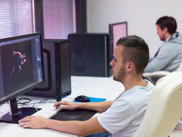 young graphic designer working at workplace. guy sitting at table retouching photo using digital tablet with pen and desktop computer indoors. freelancing and distance job concept