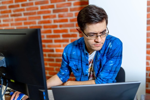 Young succesfull businessman working in office. Serious handsome man using laptop and looking into screen.