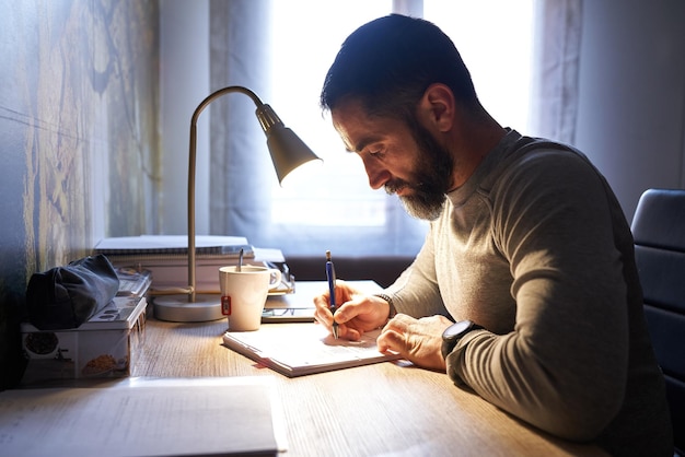 Young white man with a neat beard studying and looking at the phone at his desk