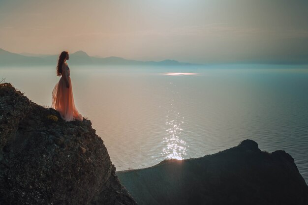 Young woman in long dress standing on a rock