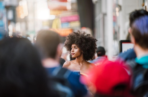 young woman looking away while holding smart phone on city street