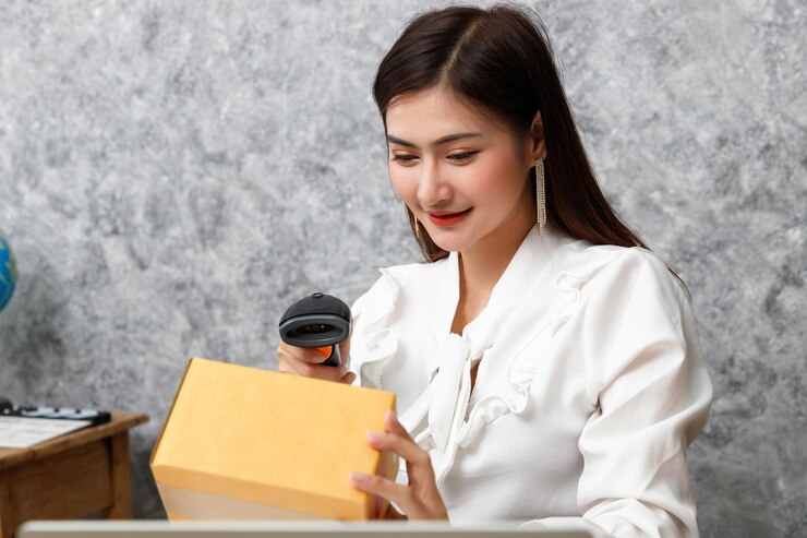 Photo young woman using bar code reader to scan package while sitting against wall
