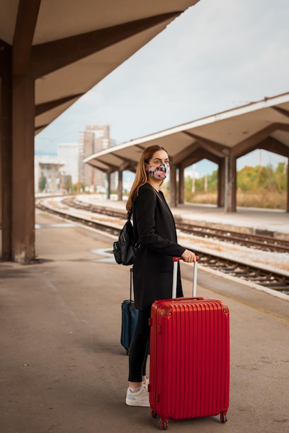 young woman wearing mask standing on railroad station platform