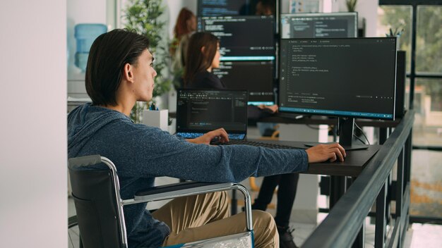 focused software developer in wheelchair writing server code in agency data room, using security system. engineer with physical disability programming user interface artificial intelligence office.