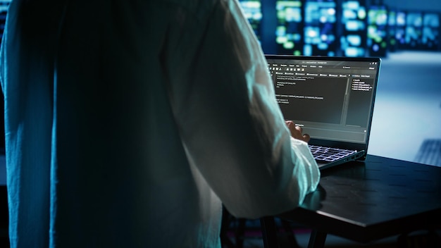 Licensed programmer running code on laptop, troubleshooting and updating data center equipment designed to accommodate server clusters, networking systems and storage arrays, close up