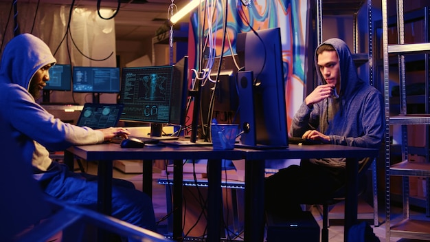 Panning shot of hackers working hard on writing lines of code on hideout computers trying all methods of getting past security systems Professional scammers building scripts that can hack devices