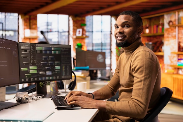 Portrait of smiling IT expert using PC in startup office to implement algorithms