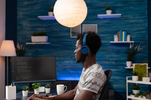 Programmer man wearing headphones typing binary code for website security working remote frrom home. African american it developer writing infographics javascript programming firewall server