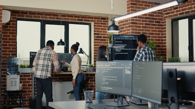 System developers analyzing code on wall screen tv looking for errors while team of coders collaborate on artificial intelligence project. Programmers working together at machine learning software.