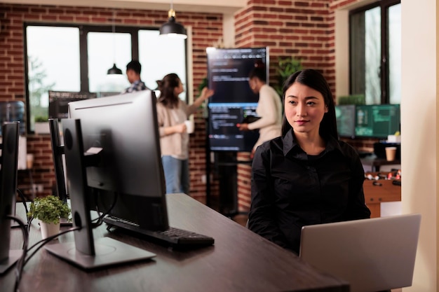 Asian programmer typing machine learning server code, sitting at desk table in it software company. Programming engineer working on database system with coding script in it developing office