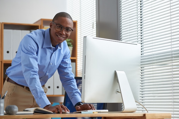 Side view of happy startupper using the computer mouth and looking at camera