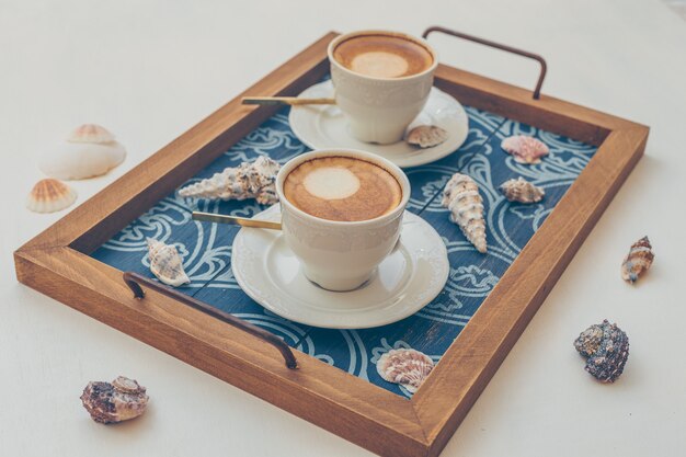 2 tasses de café dans le plateau de service avec des objets décoratifs sur blanc.