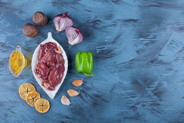 Abats de poulet sur un plateau, bol d'huile, sel, oignon, ail et poivre, sur le fond bleu.