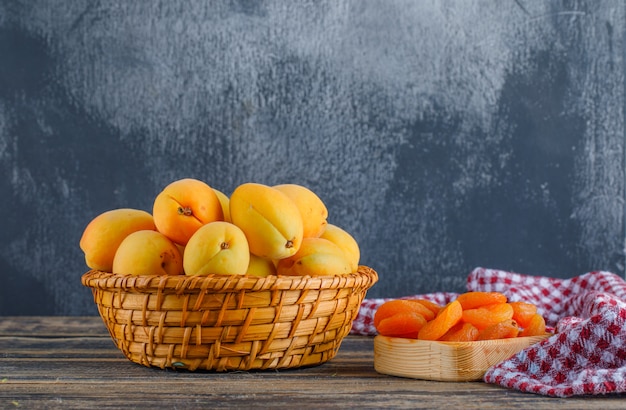 Abricots aux abricots secs, toile de pique-nique dans un panier en osier sur plâtre et table en bois, vue de côté.